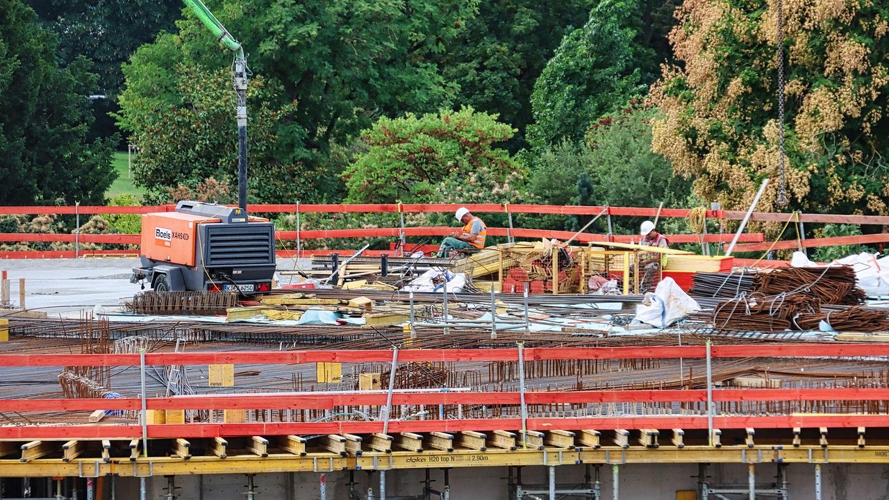 A large urban construction site with cranes and partially built structures under a blue sky.