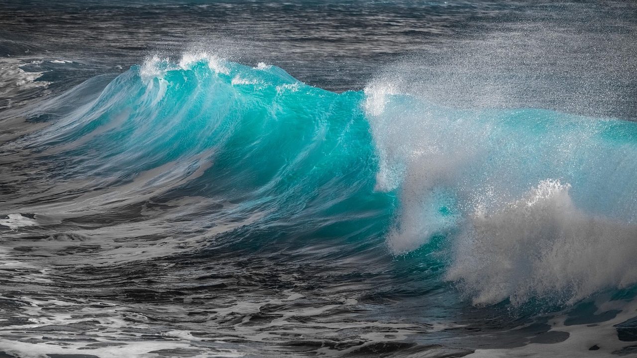 Ocean waves surging against a low coastal walkway during an exceptionally high tide.
