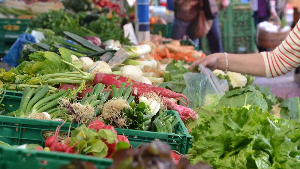 Colorful produce and craft vendor stalls fill an open-air weekend farmers market.