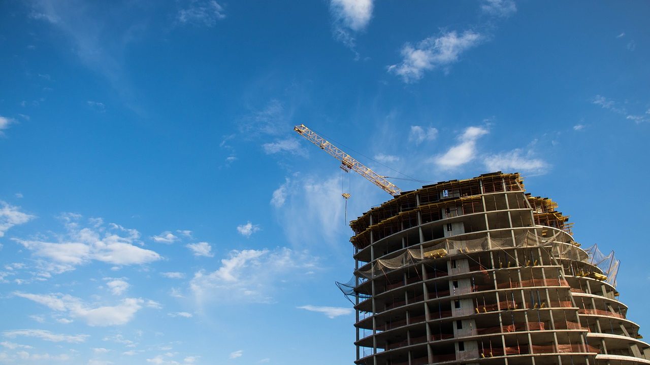 Construction cranes rising above a partially built apartment complex in an urban neighborhood.