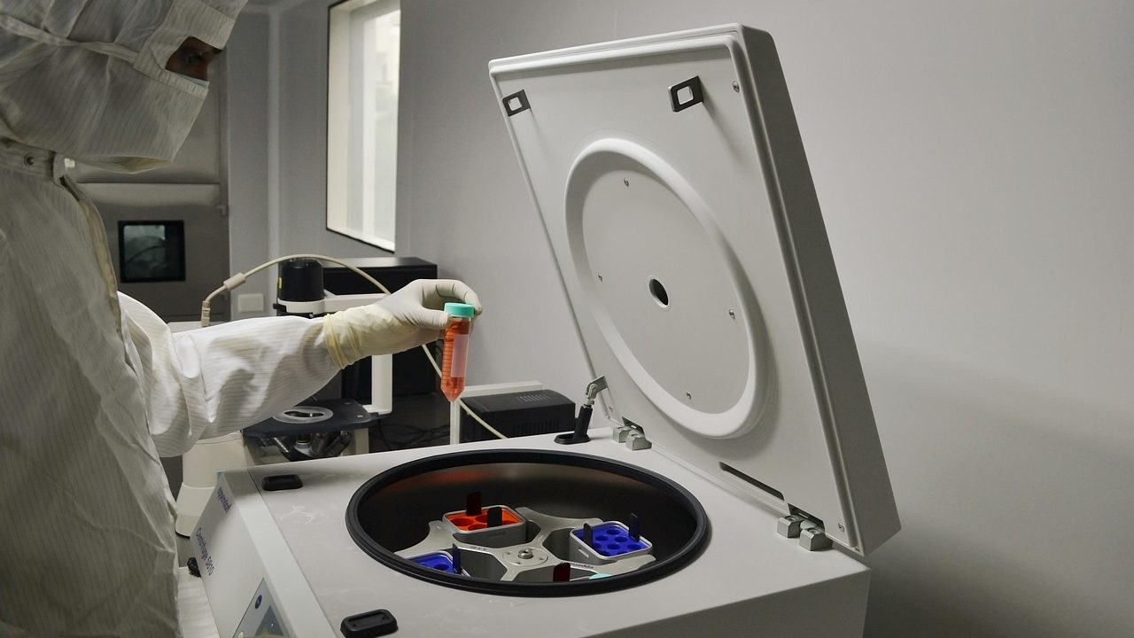 Scientists working at laboratory benches with microscopes and equipment under bright lights.