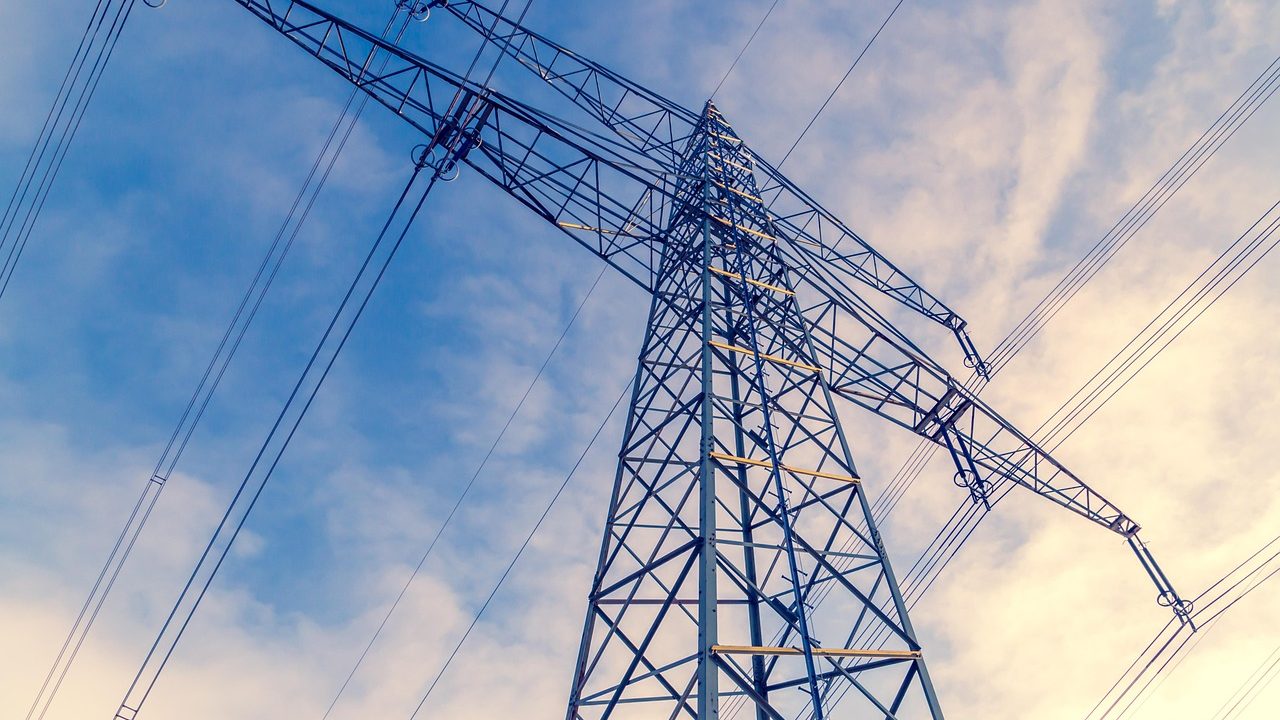 A row of tall steel electricity transmission towers stretching across an arid inland landscape.