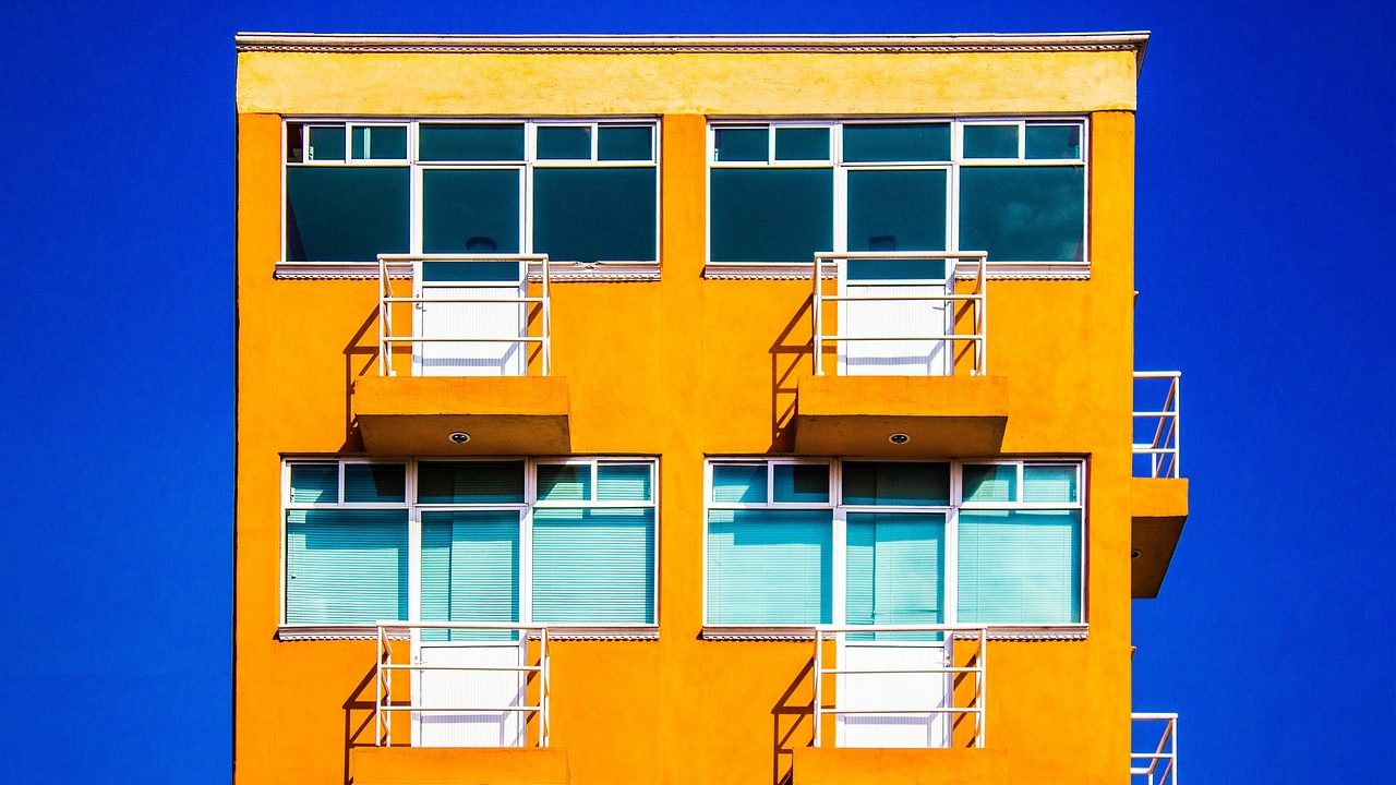 A modern multifamily apartment complex viewed from a parking lot on a sunny day.