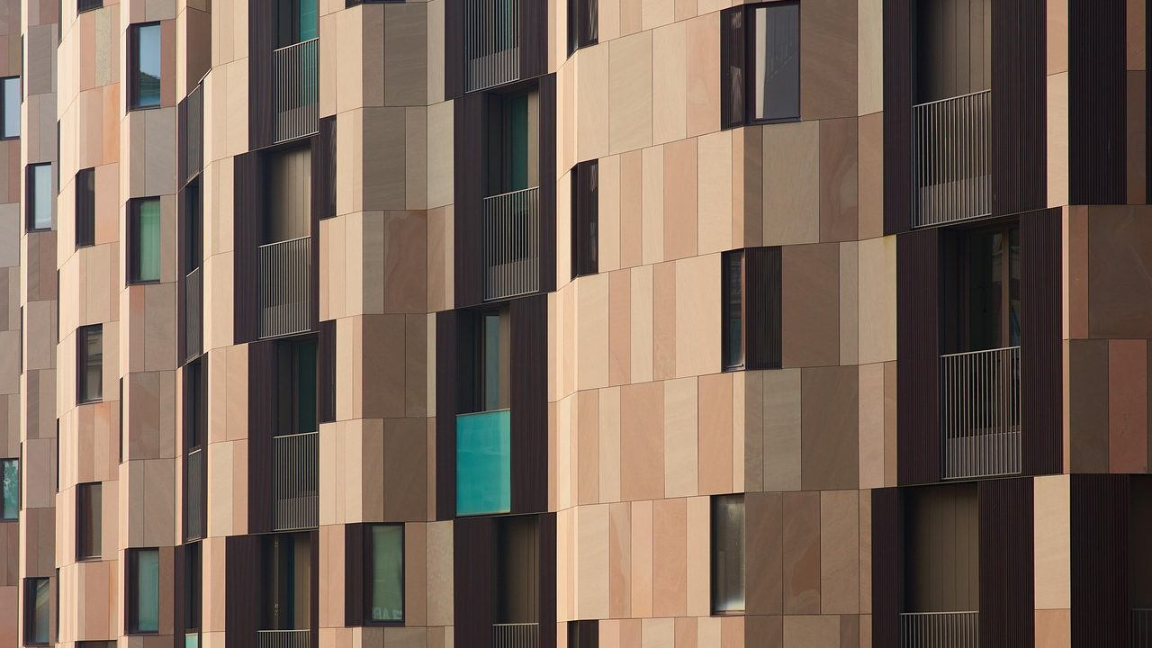 Modern multi-story condominium building facade with balconies under bright sky.