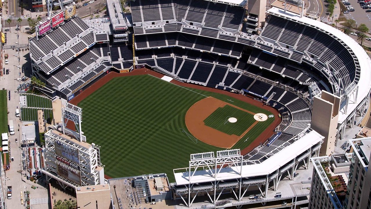 Rows of empty blue stadium seats inside a modern baseball park on a sunny day.