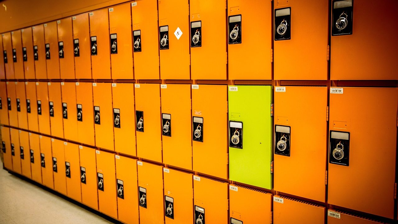 An empty school hallway lined with lockers under fluorescent lighting between class periods.