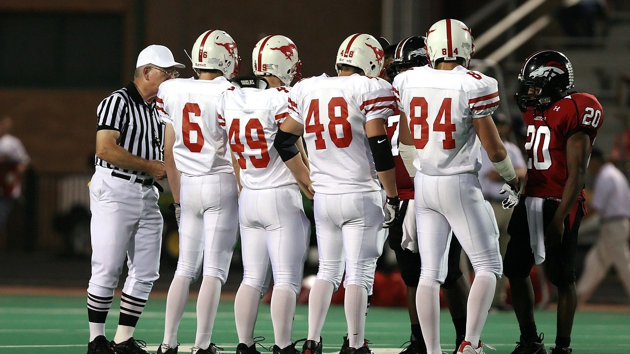 Stadium lights illuminate a high school football field at night, end zone visible.