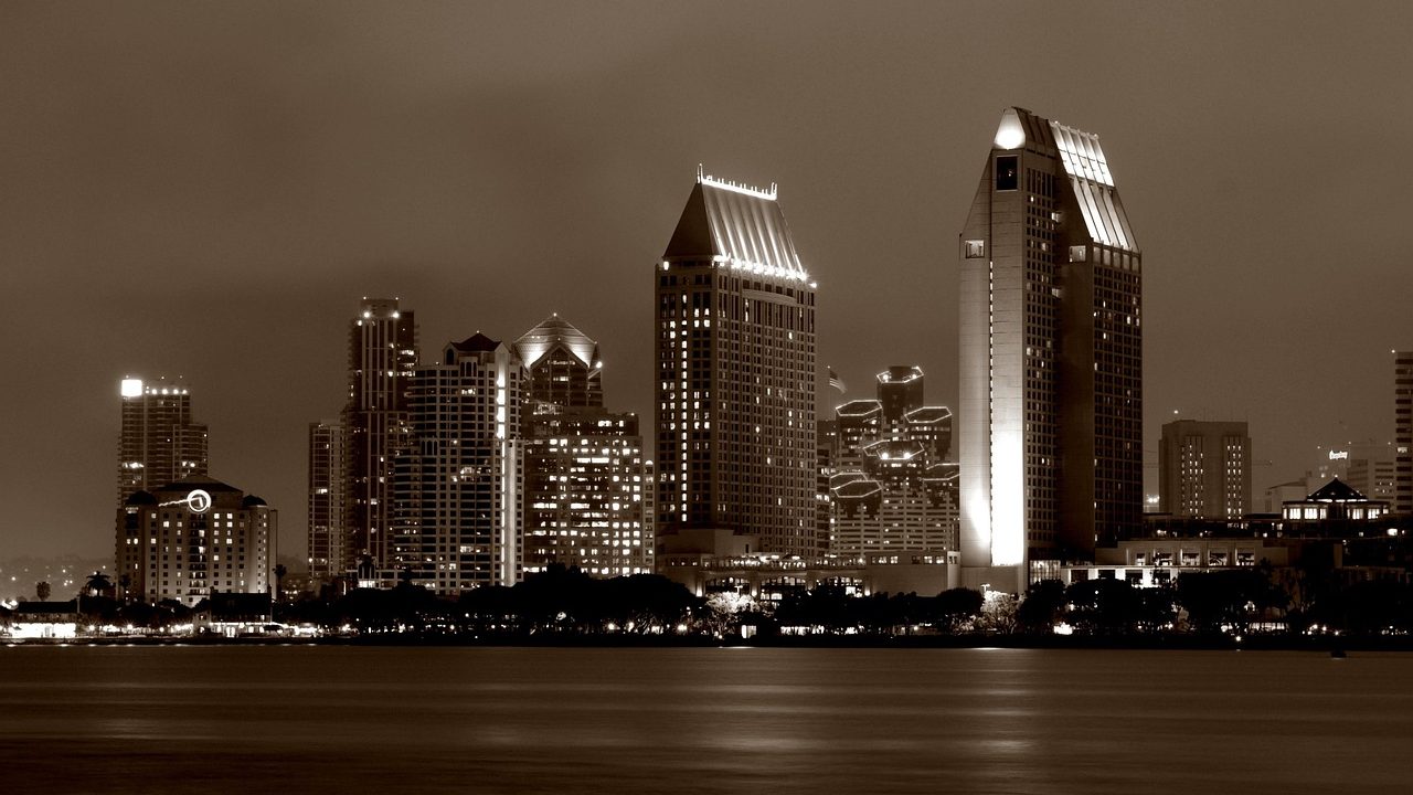 Panoramic view of a sunny urban skyline reflected in calm harbor water.