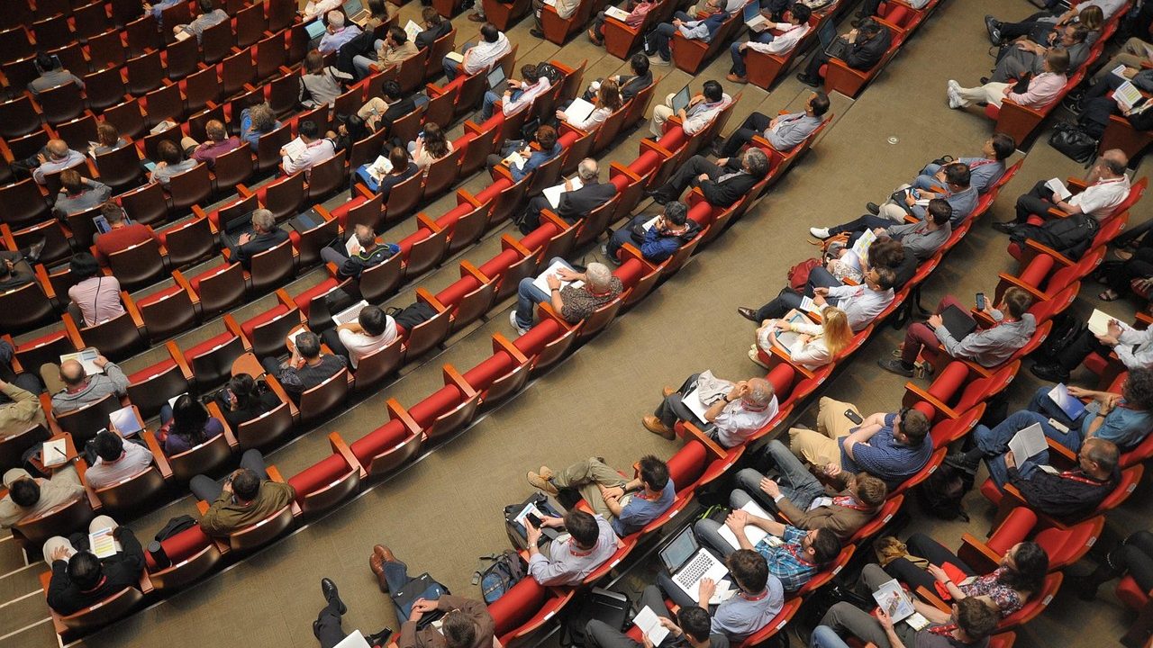 Empty municipal council chamber with tiered seating, microphones, and overhead lighting.